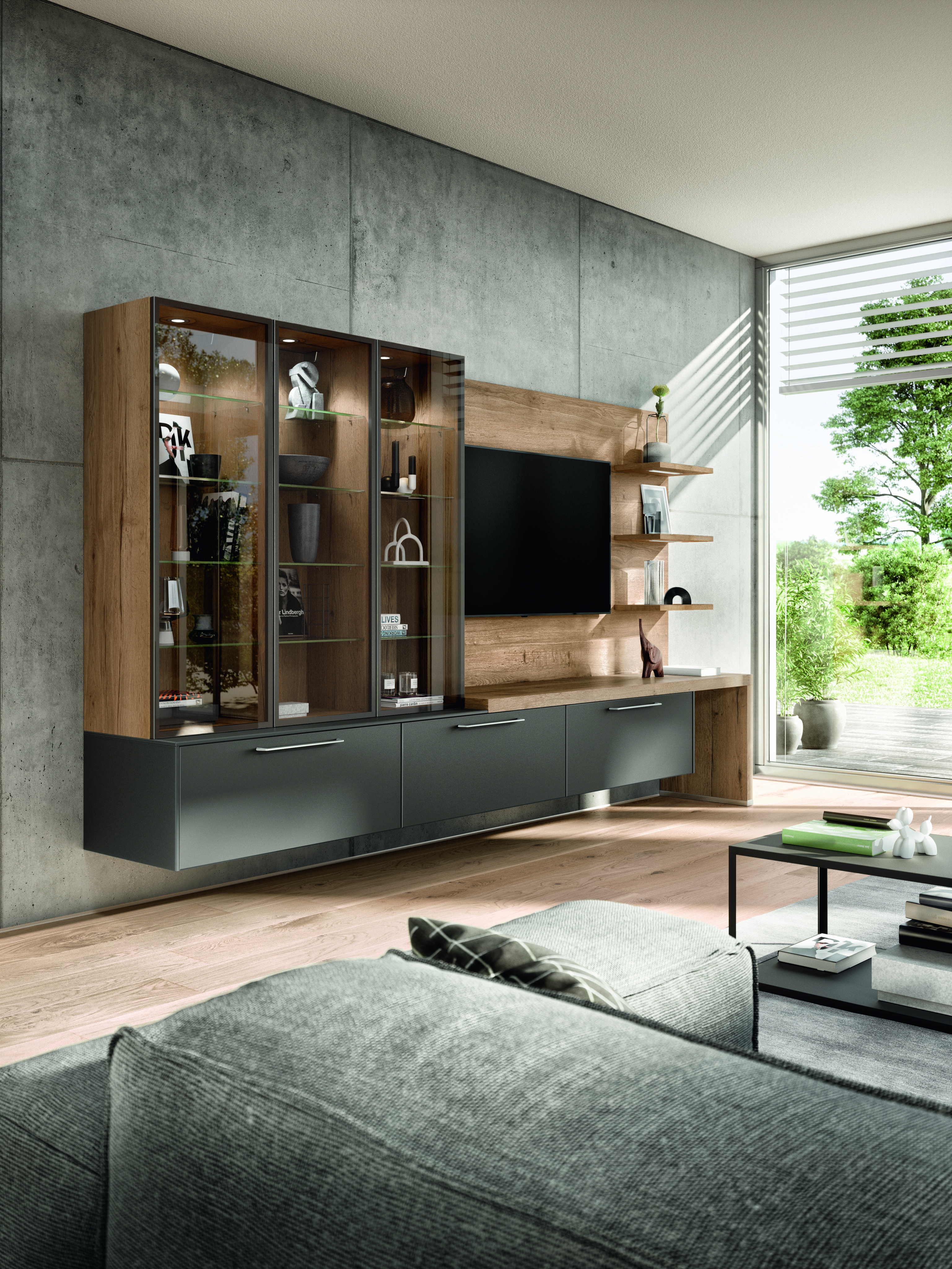 Modernes Wohnzimmer mit grauem Sofa, TV-Wand und großen Fenstern mit Blick ins Grüne.